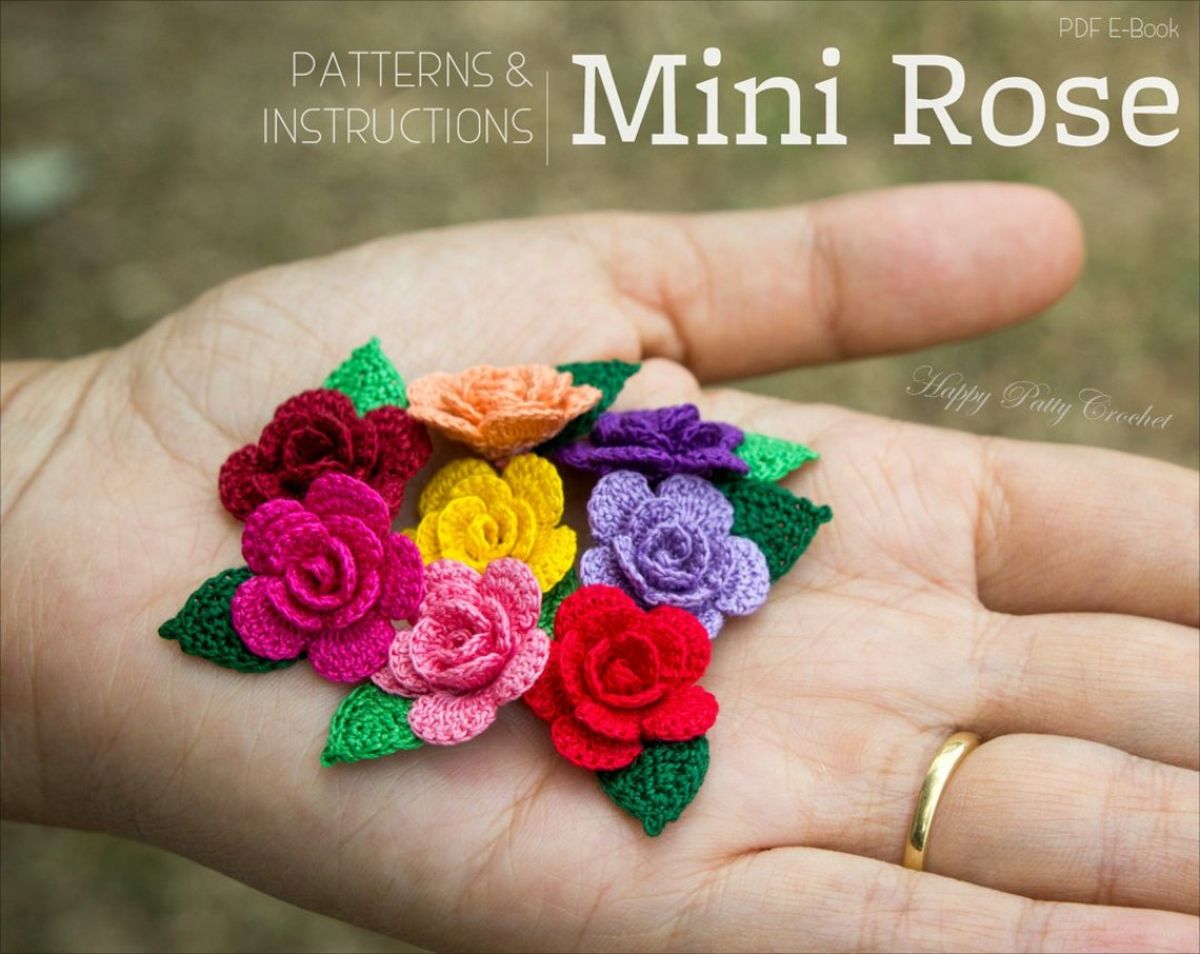 An outstretched hand holding small red, pink, yellow, and purple crochet roses with small green leaves attached to each rose.