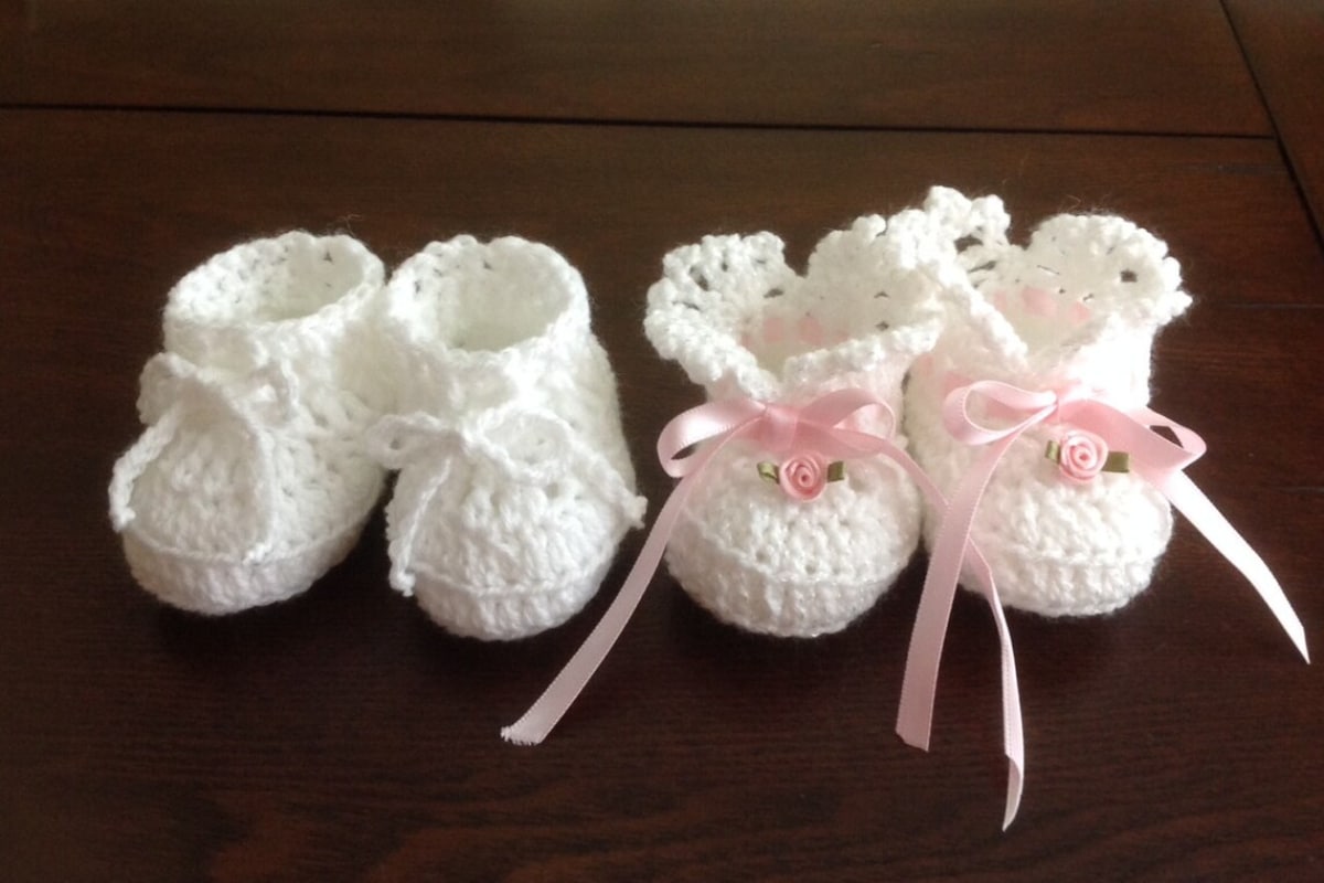 White crochet baby booties for newborns. One set with white bows in the center and the other has pink silk bows.