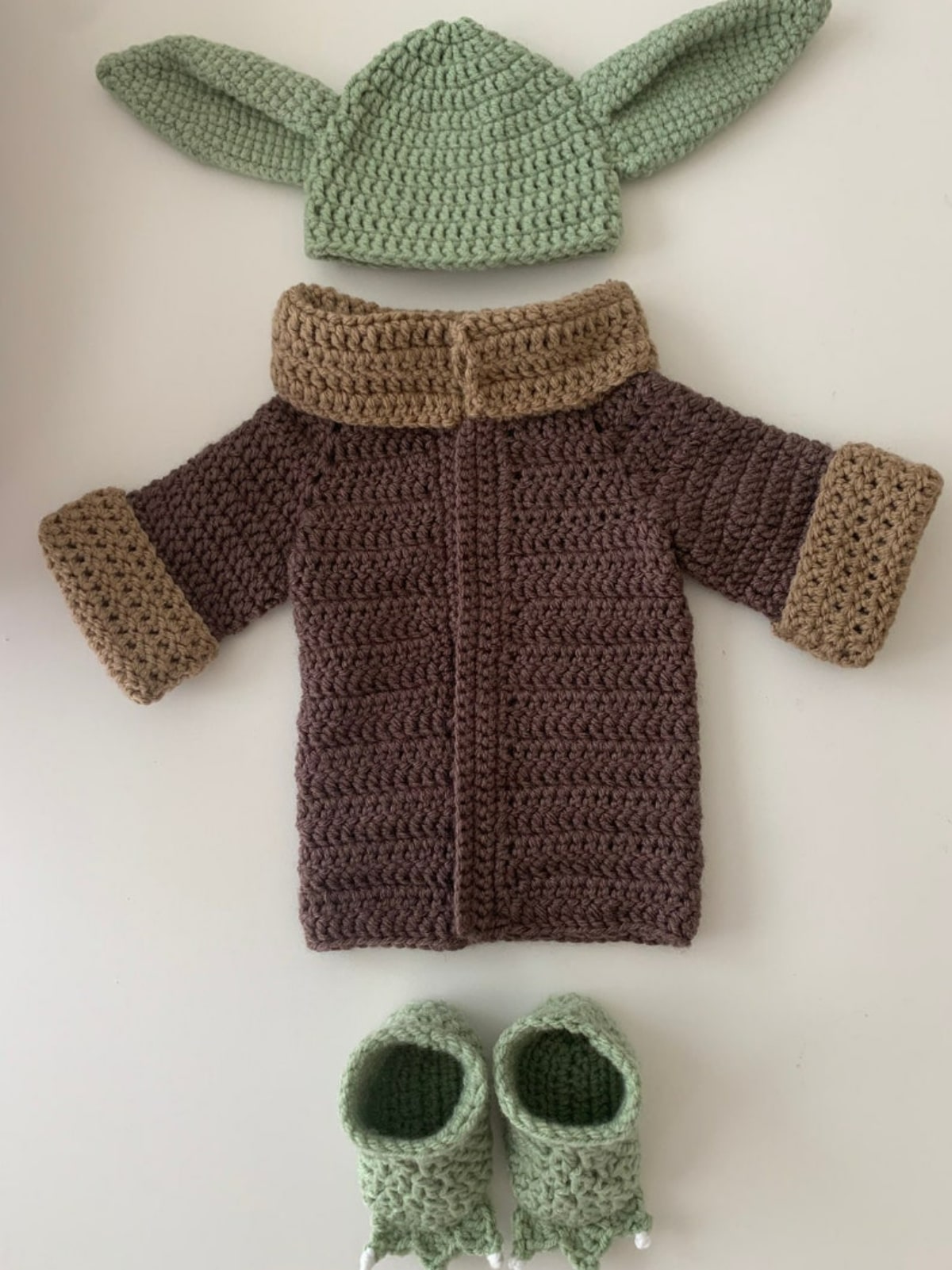  Newborn crochet baby Yoda costume with a green hat, dark brown robe, with a light brown collar and cuffs, and green booties with white claws.