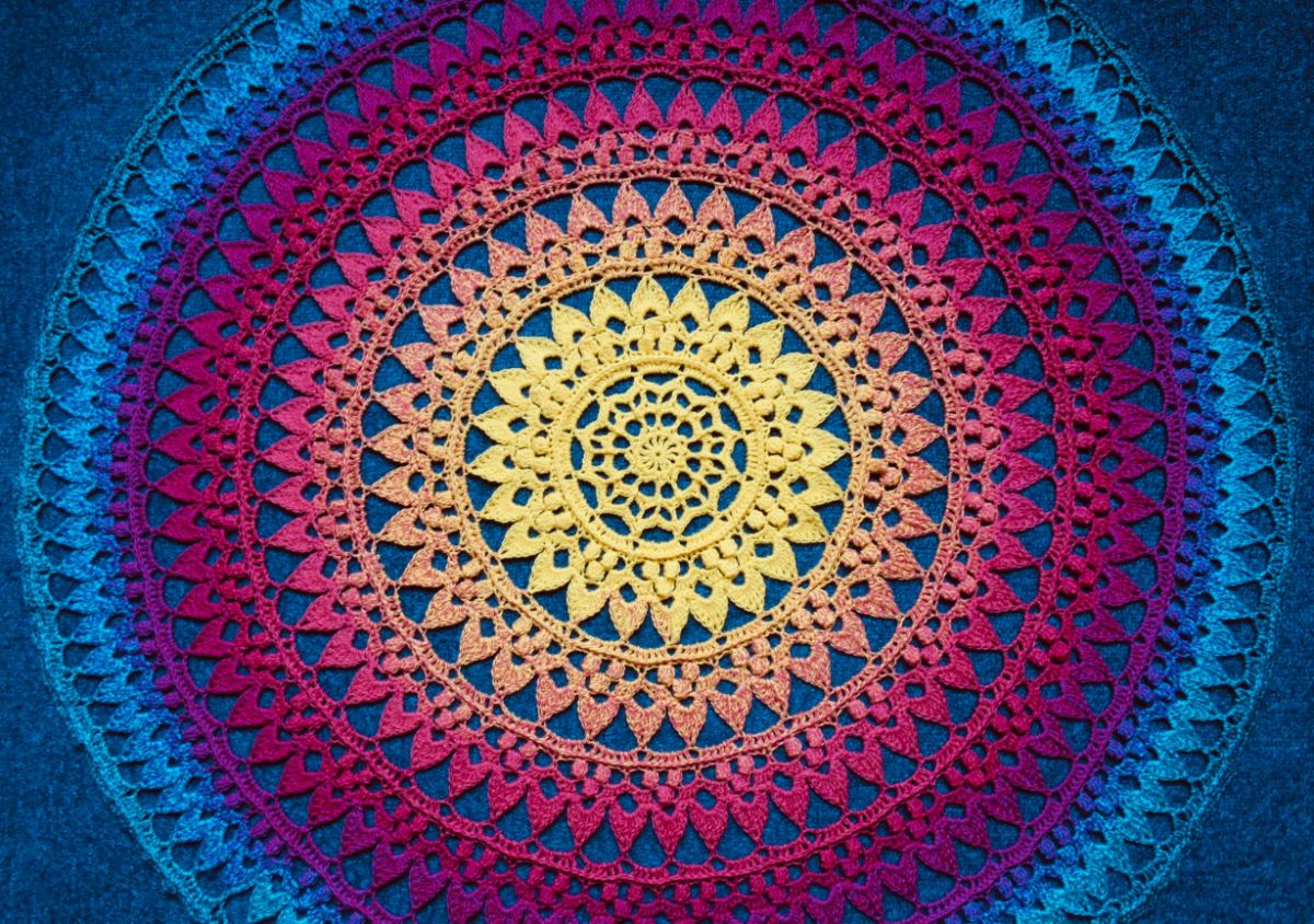 A brightly colored blue, purple, pink, and yellow round mandala with each row having a different color on a dark blue background.