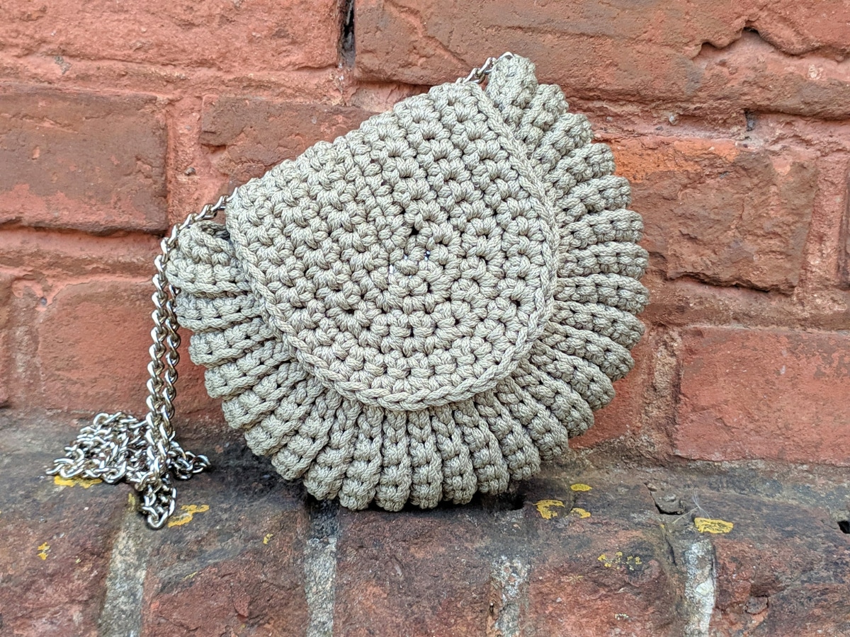 Pale green crochet purse with a flap over the front to fasten it and a thin strap on the left side.