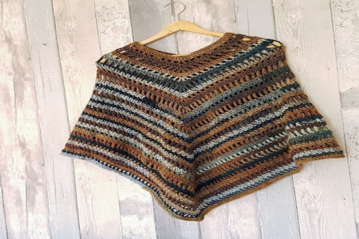 A brown, black, and grey horizontal striped poncho with a round neck on a pale wooden hanger on a wooden background. 