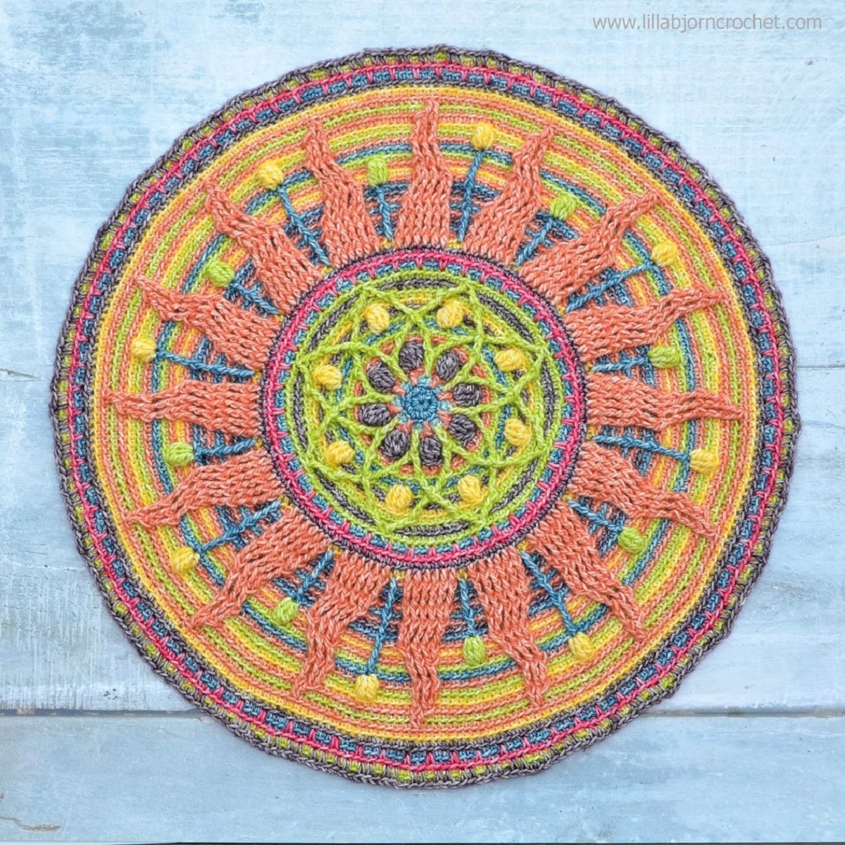 A round crochet mandala with a large yellow flower in the center and light orange petals spreading out to the edges of the circle.