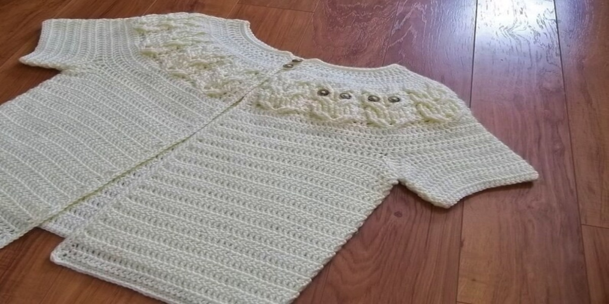 White short sleeved crochet cardigan with a semi circle of cream owls with black eyes stitched along the chest.