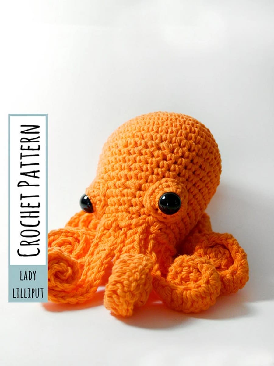 Large stuffed orange crochet octopus with two black eyes and curled orange tentacles on a white background.