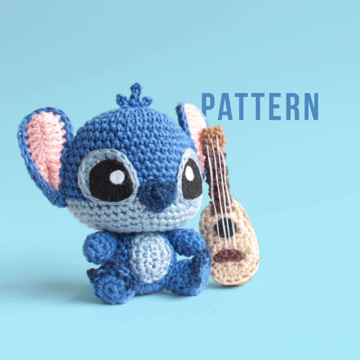 Small crochet Stitch with an oversized head sitting on a blue background next to a crochet ukulele. 