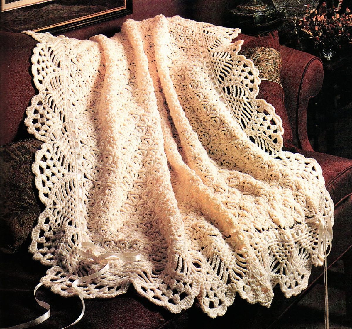 Light pink Victorian style crochet baby blankets with a large lace trim on all sides draped over a couch.