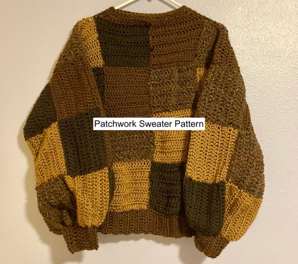 A brown and yellow long sleeved crochet patchwork sweater with a round neckline and cuffed sleeves on a hanger.
