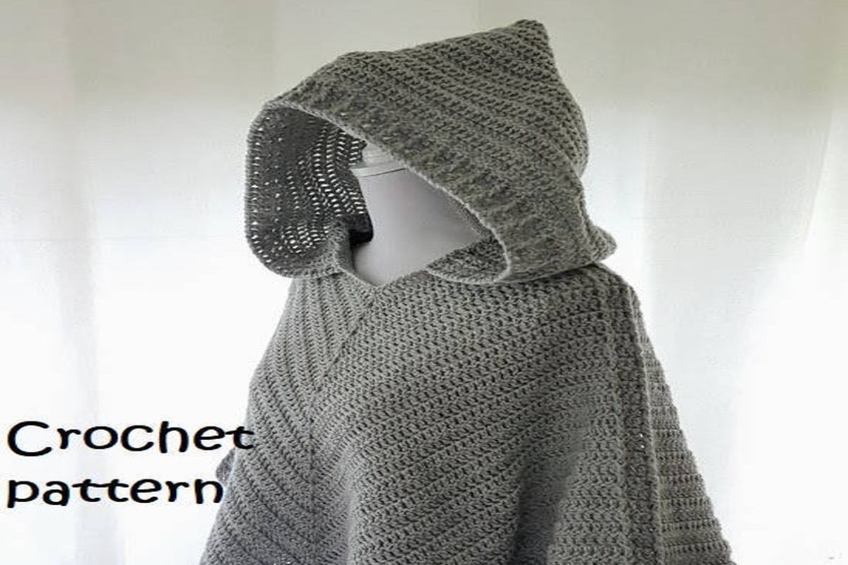 A chunky knit pale green poncho with dark green stitching on the side. The poncho features a large pale green hood too.