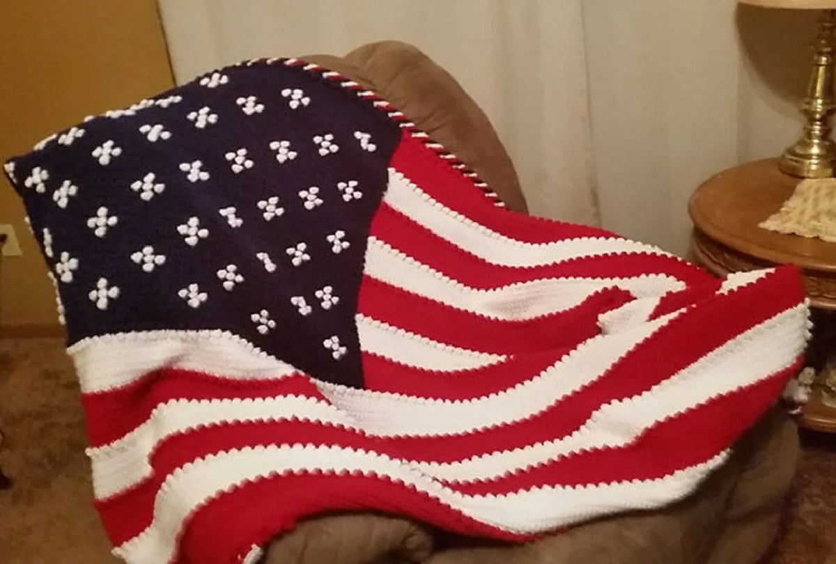 Crochet blanket of American flag with crosses instead of stars spread across a brown leather chair.