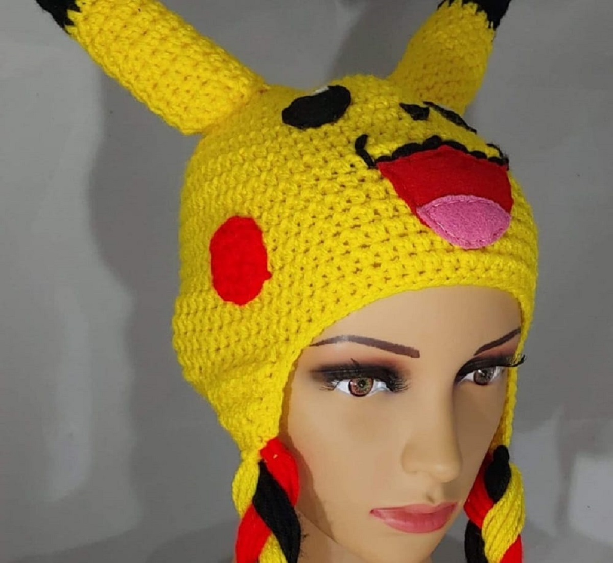 Mannequin head wearing a crochet Pikachu beanie with its tongue sticking out and braids coming down either side of the hat.