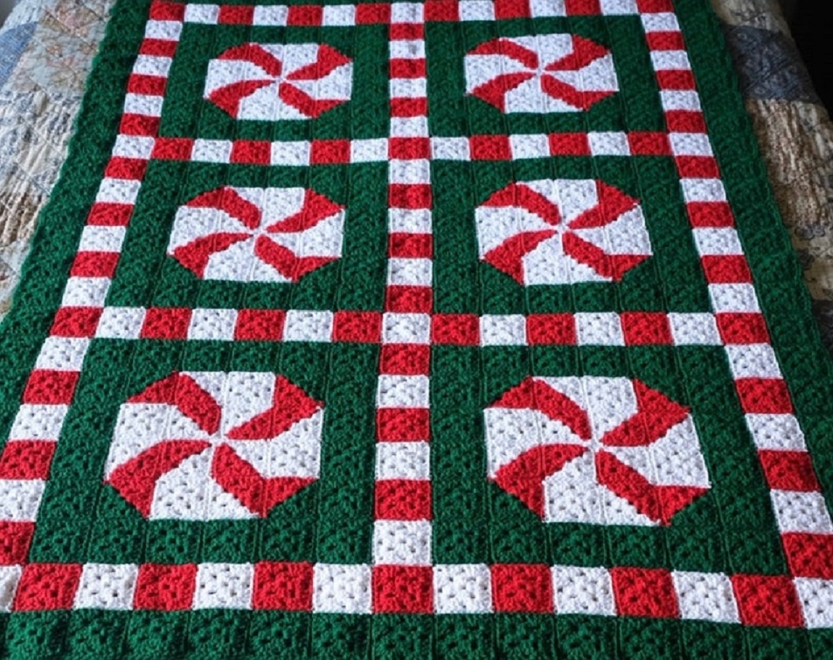 Green crochet Afghan with a red and white square border around pixelated red and white peppermint swirls. 