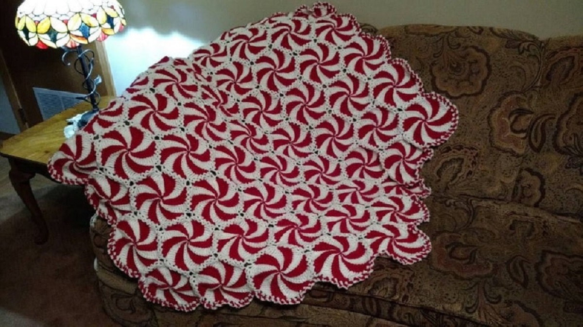 Large textured peppermint crochet Afghan with red and white swirls all over draped over a brown couch.