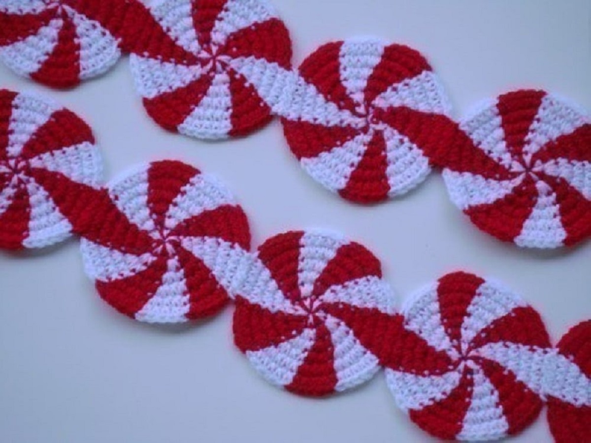 Small white crochet circles with red swirls throughout stitched together to make a scarf on a white background.