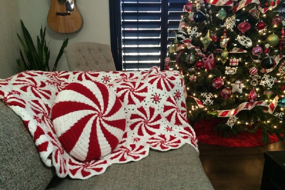  White crochet planet with red and white peppermint style swirls all over and a red and white swirl cushion on top next to a Christmas tree.