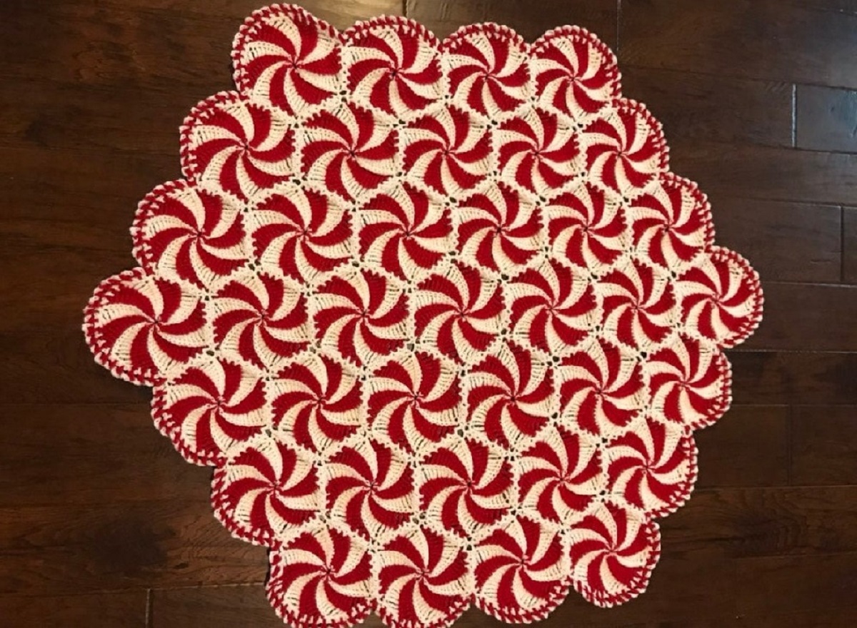 Large red and white crochet throw made up of round circles of red and white swirls on a dark wooden floor.