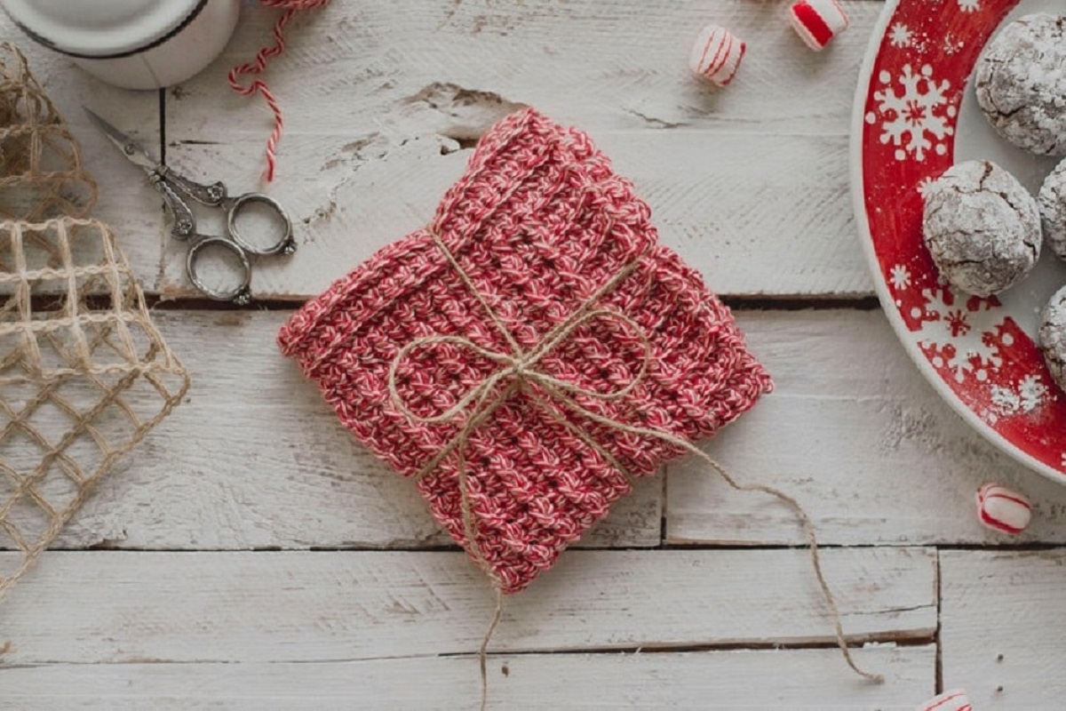 A light red waffle stitch crochet square with brown string tied into a bow on a light wooden background.