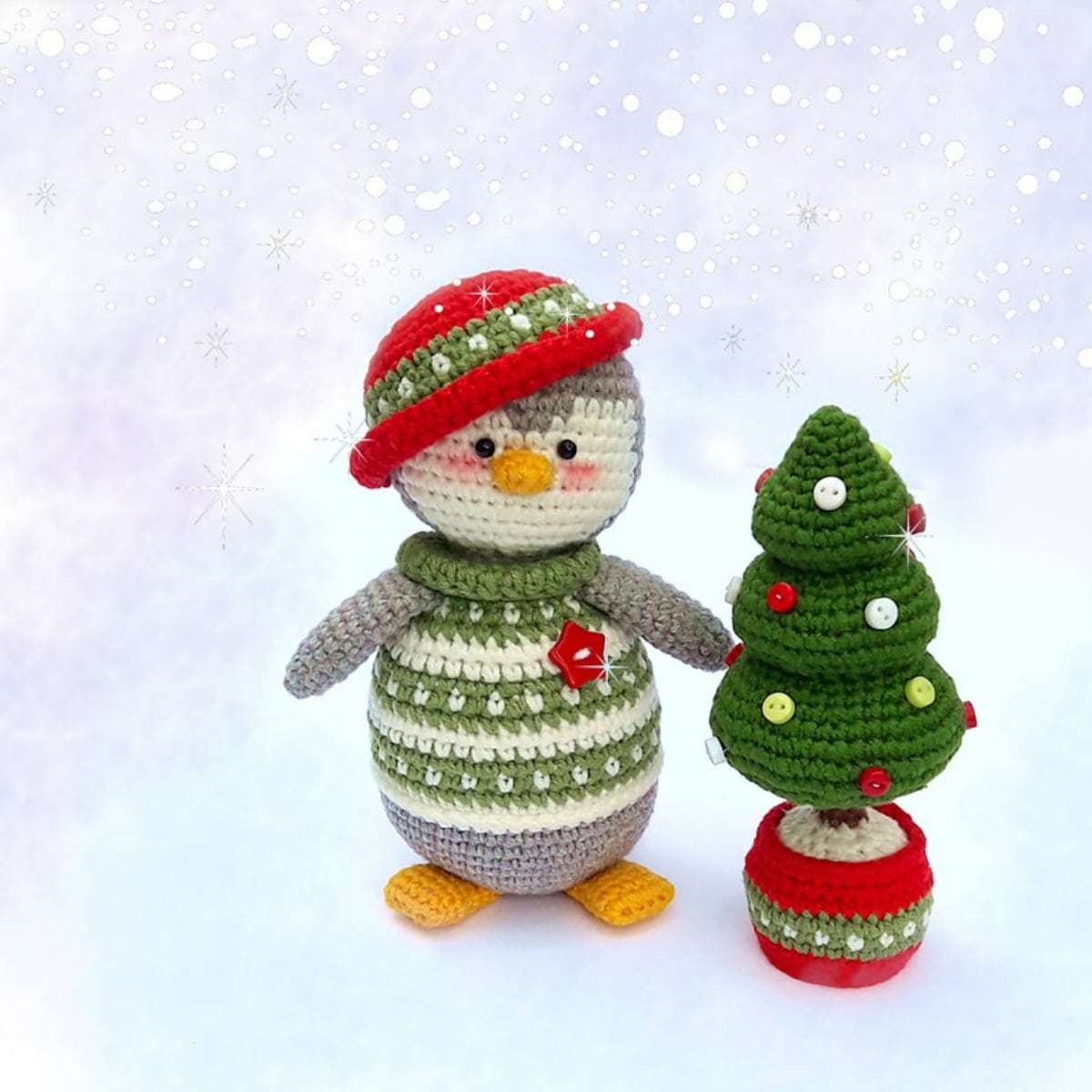Small crochet penguin in a green and cream striped jumper with a red bowler hat standing next to a small crochet Christmas tree in a red bucket.