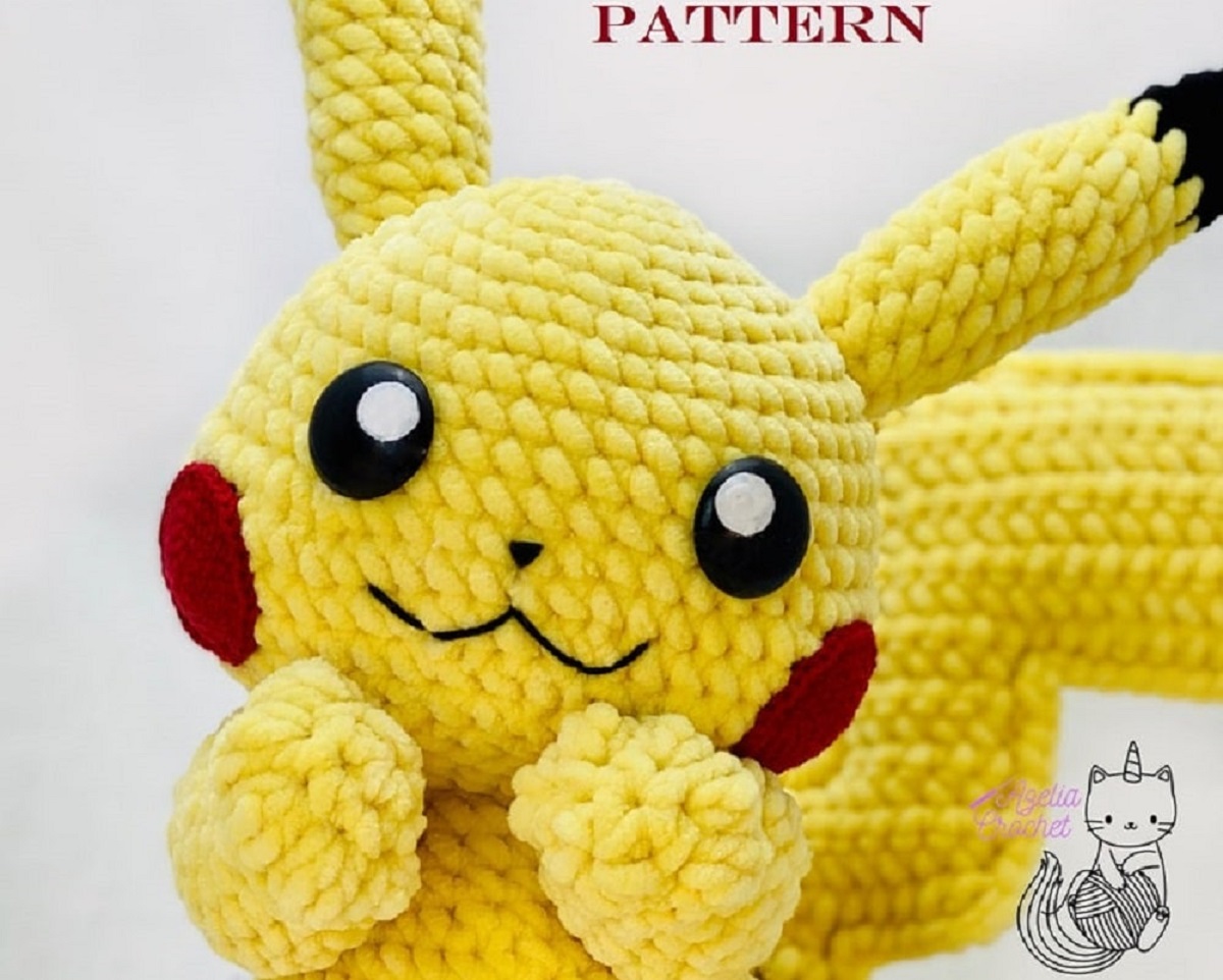 Large crochet Pikachu with red cheeks and a yellow body, smiling with its hands touching its chin. 