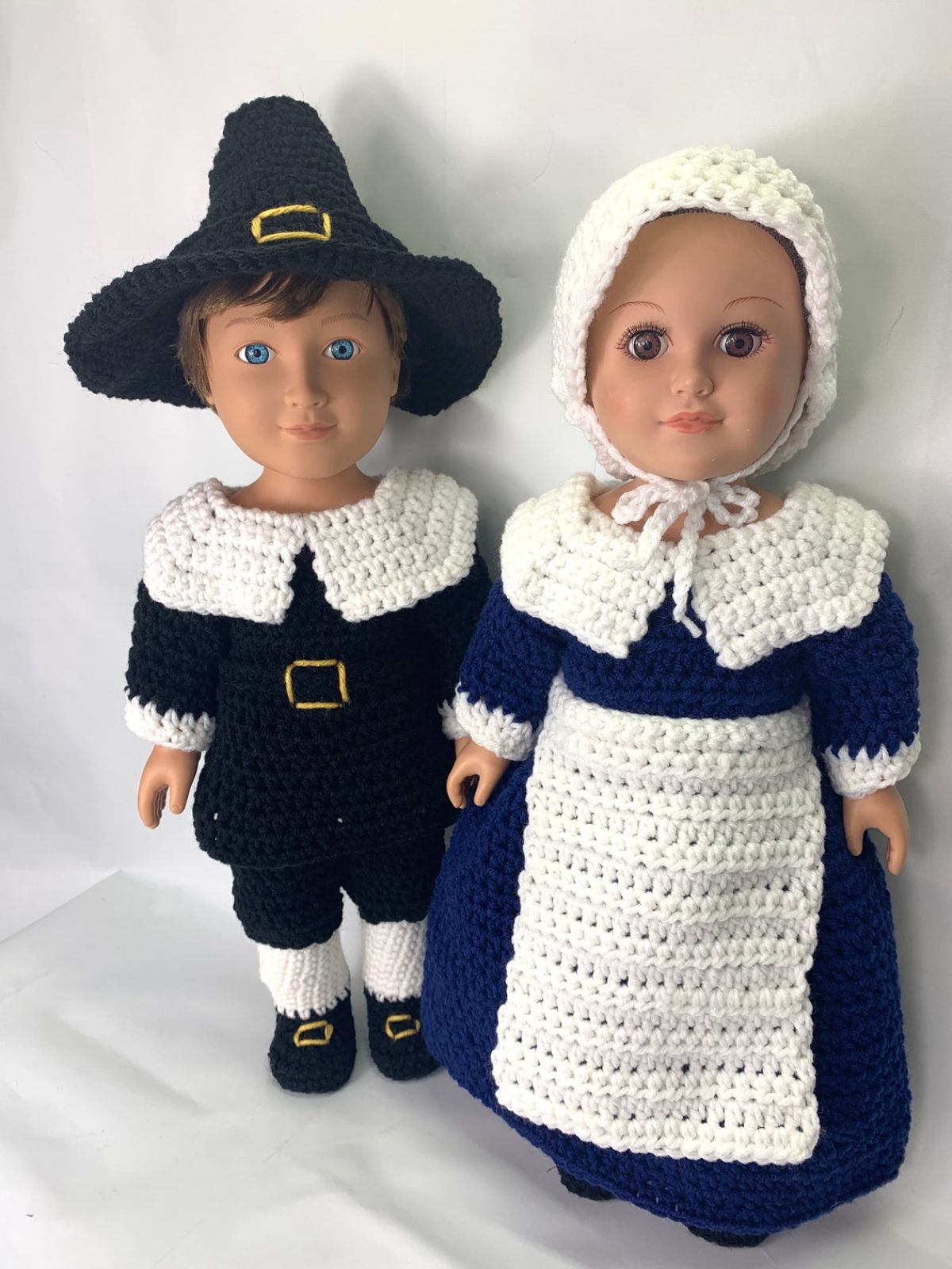 A male and female doll wearing traditional crochet pilgrim outfits standing next to each other on a white background.
