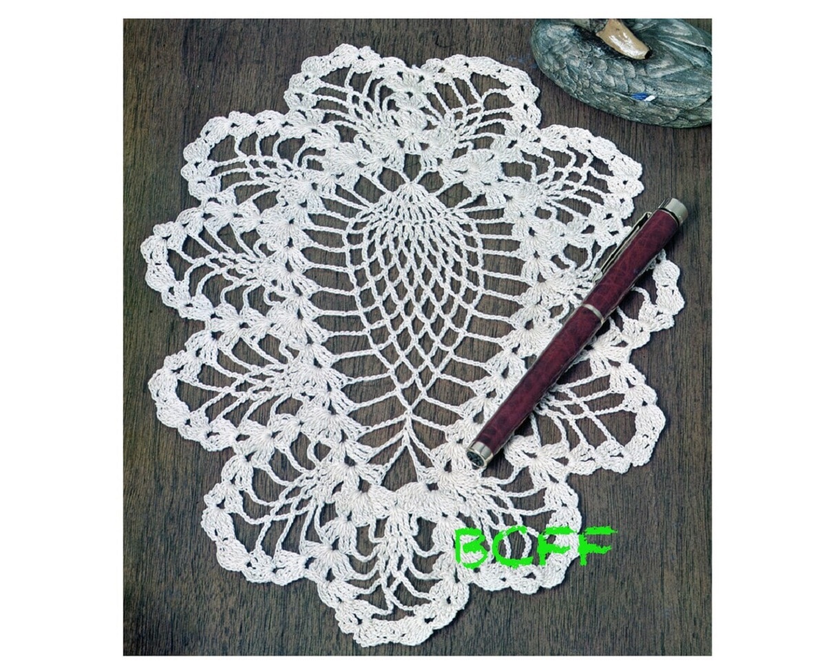  Cream crochet doily with a pineapple in its center with a purple pen on top of it laid on a wooden table.