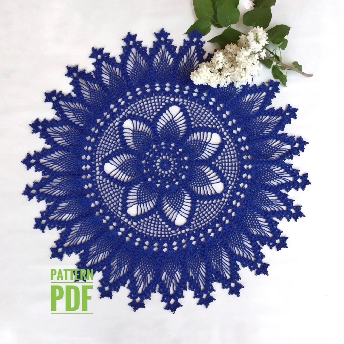 Navy blue crochet doily with a flower in the center of a circle surrounded by pineapples stitched into petals on a white background.