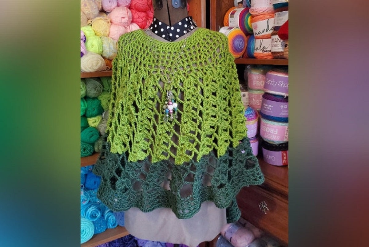Mannequin wearing a green crochet poncho with a thick dark green stripe around the bottom of the poncho.