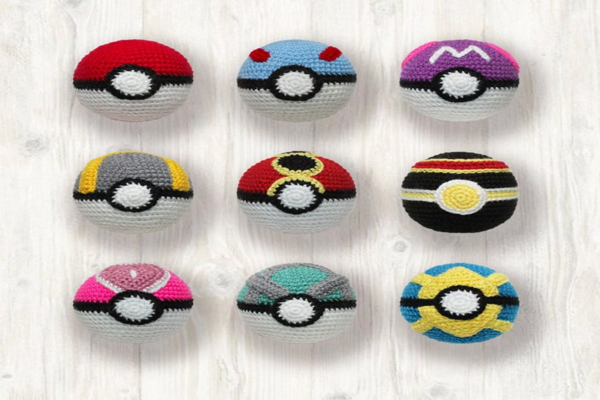 Nine crochet Pokemon balls in red, blue, pink, purple, gray, blue, and green on a light wooden background.