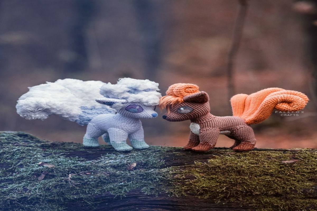 Crochet Kanto with a brown body and orange tail and hair and white and pale purple Alolan standing on a log facing each other.