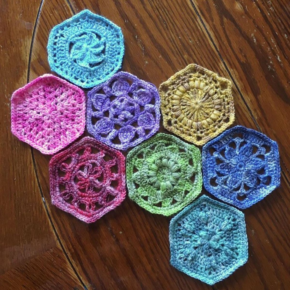 Brightly colored hexagon crochet squares with small flowers stitched into them used for baby’s blankets on a dark wooden background. 
