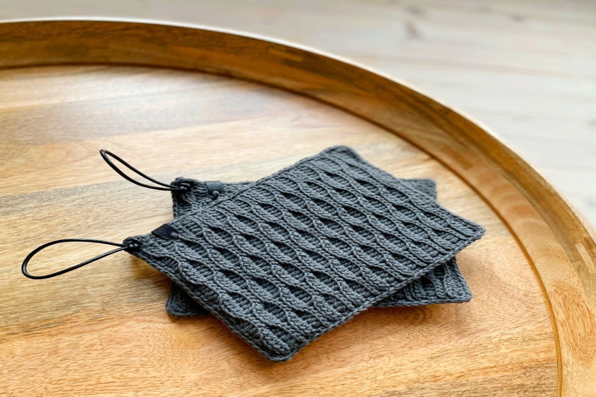 Two small gray crochet pot holders stacked on top of each other on a wooden table. 