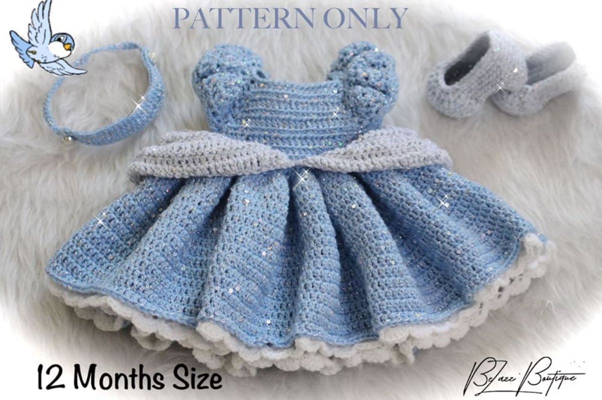 Baby crochet Cinderella ballgown in pale blue with silver detailing, crochet silver slippers, and blue tiara on a white blanket. 
