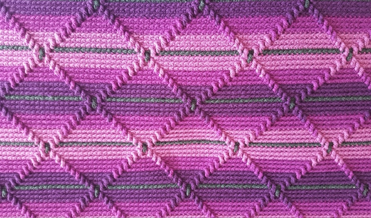 Light purple, dark purple, and green striped crochet blanket with a pink and purple diamond pattern on top.