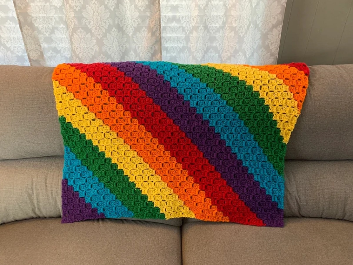 Small rainbow blanket with diagonal stripes in the colors of the rainbow in the middle of a cream sofa. 