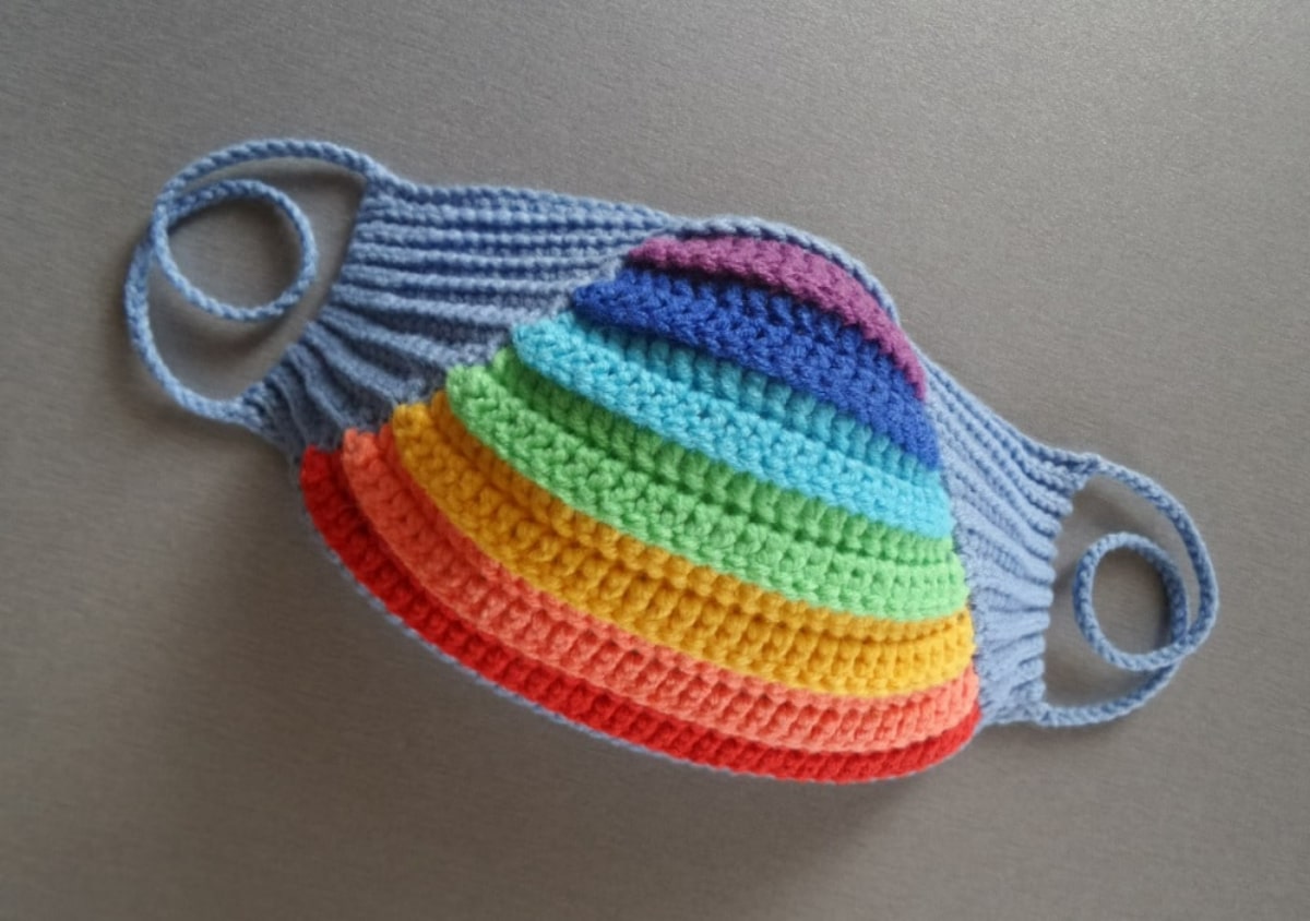 Crochet face mask with horizontal rainbow stripes in the center and gray yarn around the sides and gray loops for your ears.