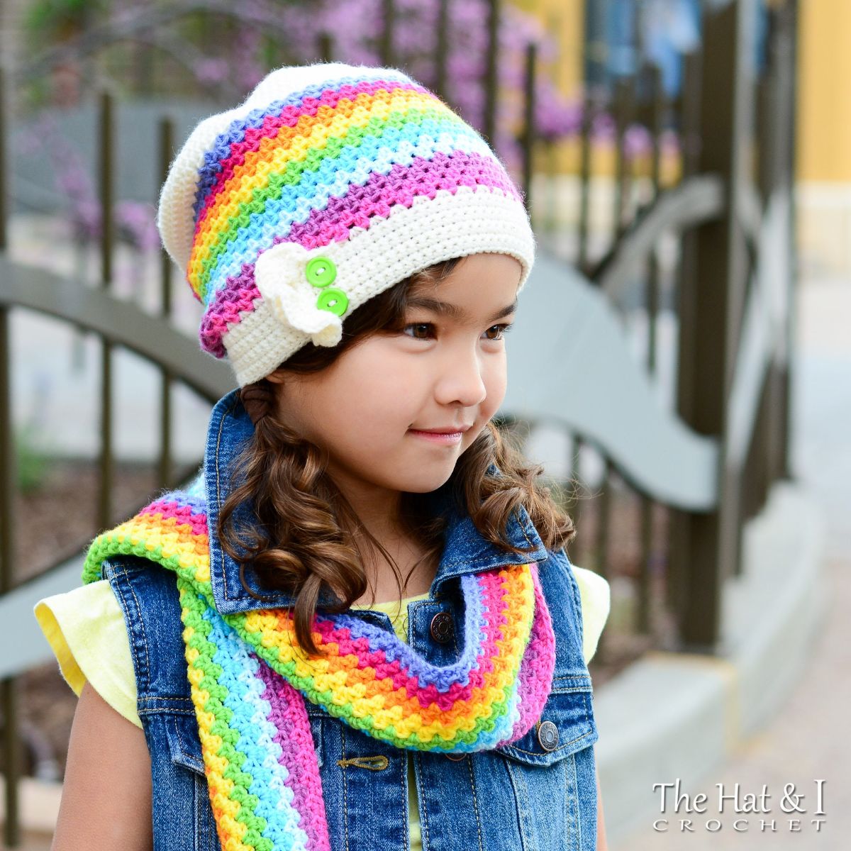 Brunette girl side facing wearing rainbow colored horizontally striped crochet beanie hat and matching scarf.