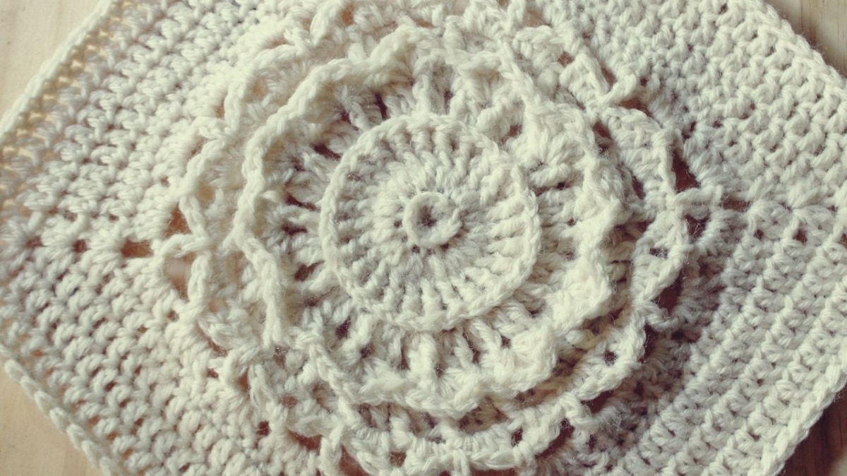 White crochet granny square with a raised applique style circle in the center with a lace trim around the circle.