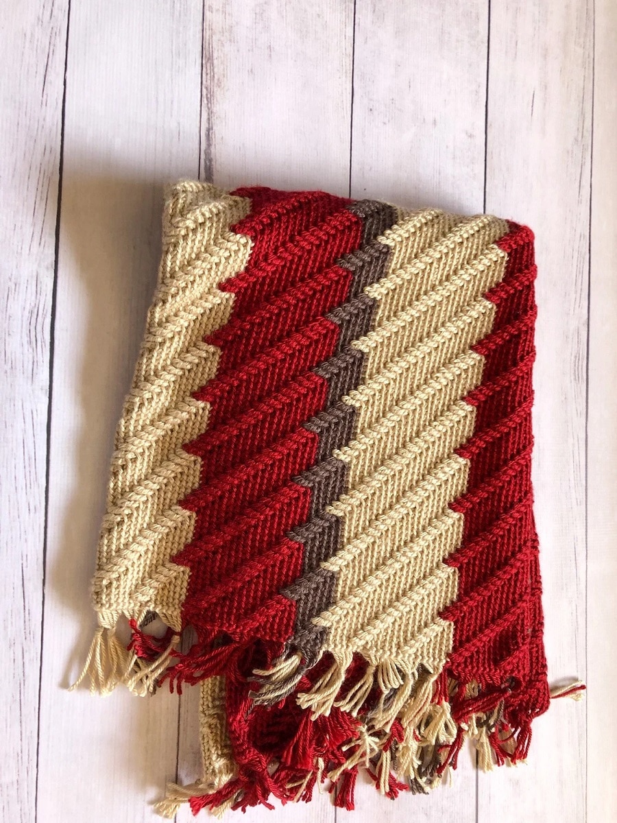 A red, yellow, and brown apache style crochet blanket with a trail of tears pattern and tassels along the bottom.