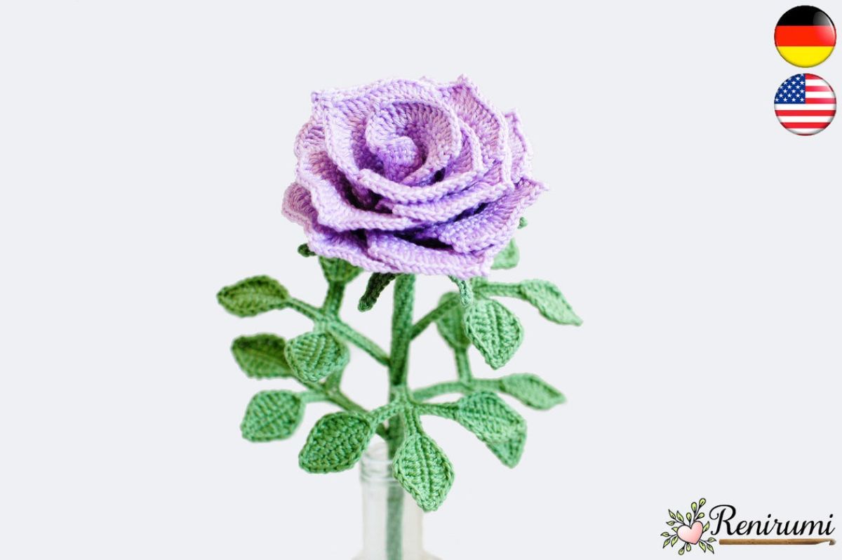 A purple crochet rose with four stems shooting off covered in small green leaves on a white background.