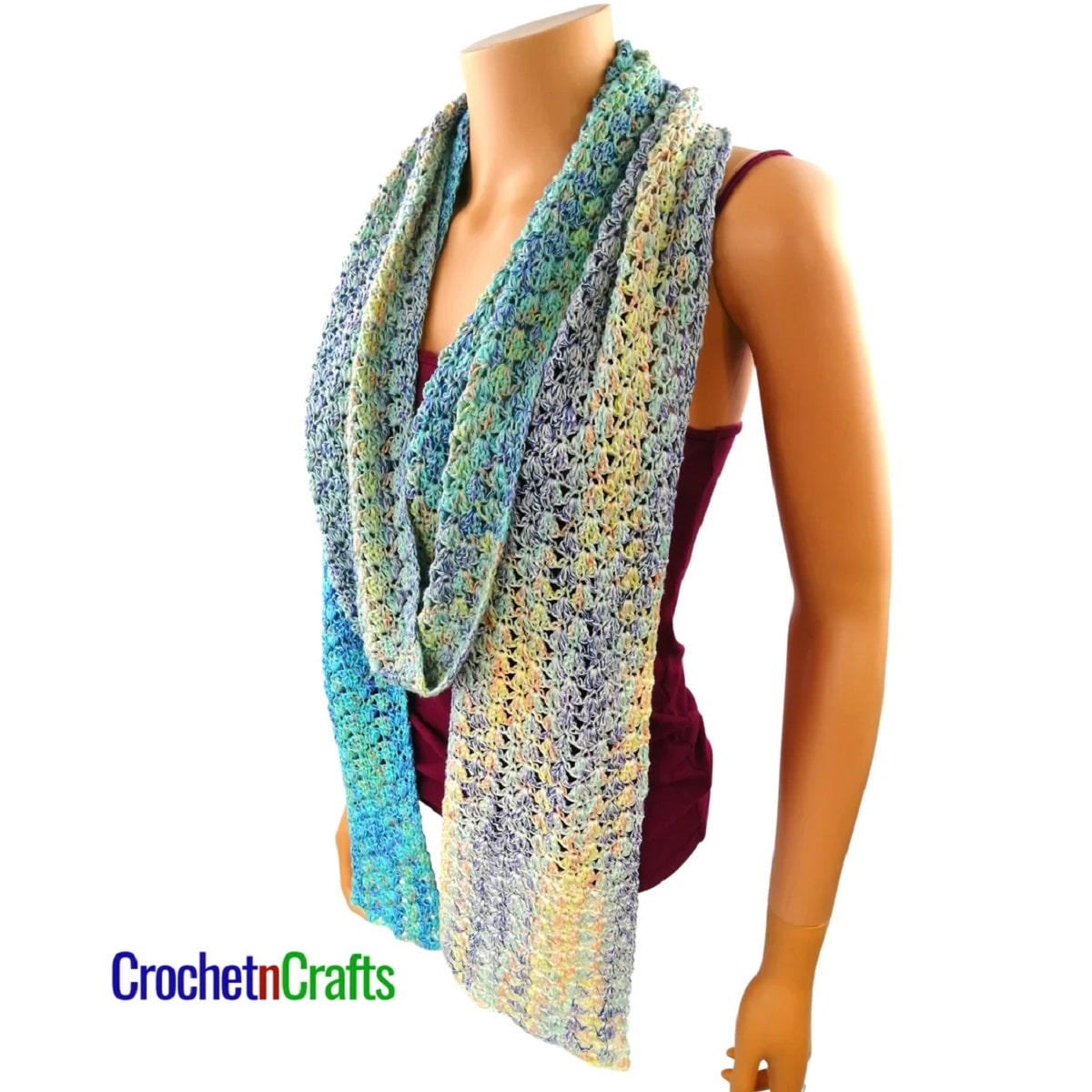 Mannequin wearing blue, purple, and green crochet scarf wrapped around its neck on a white background.