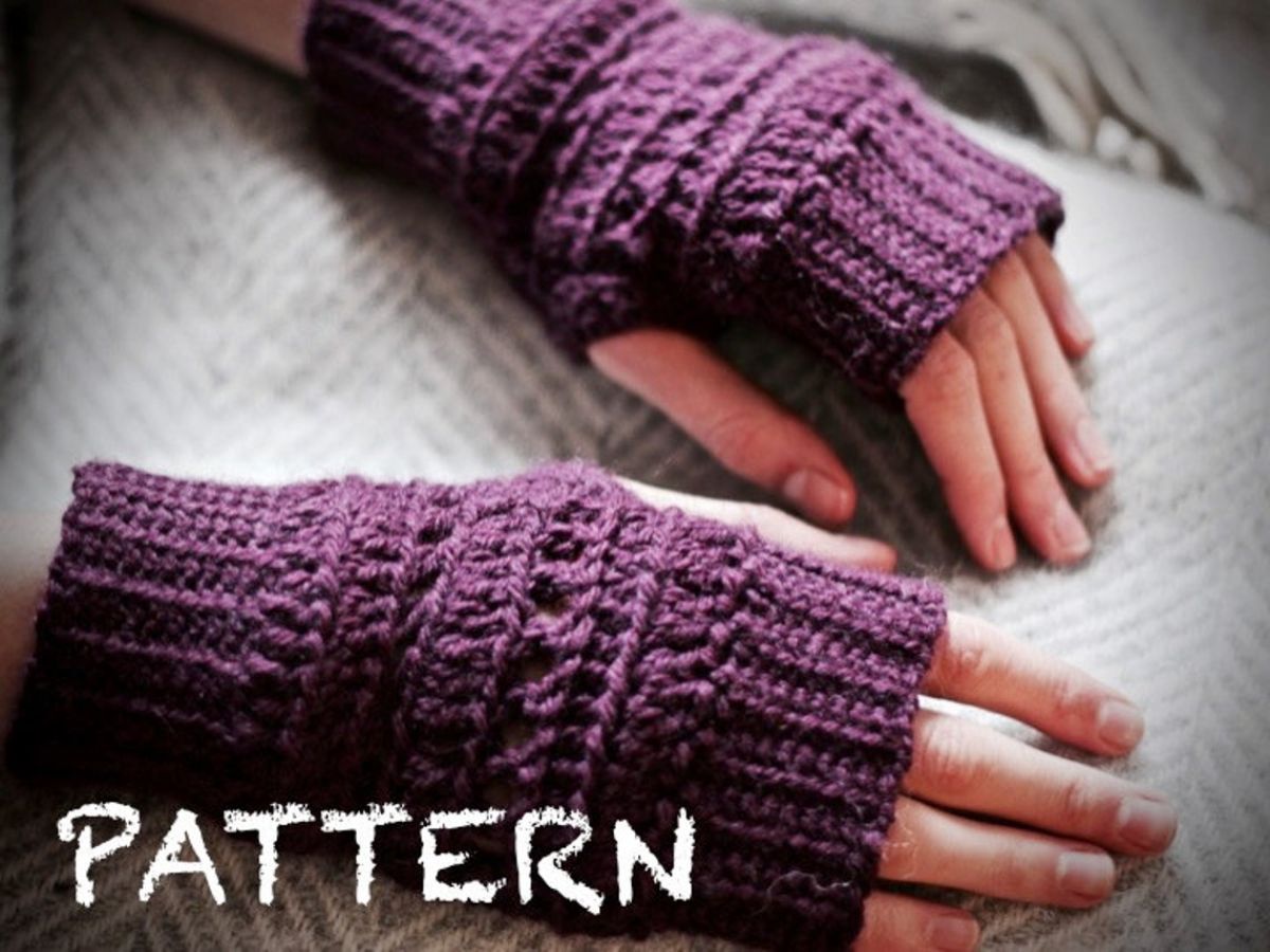 Hands wearing ribbed crochet dark purple fingerless gloves with a skein design. The gloves and hands are resting on a gray background.