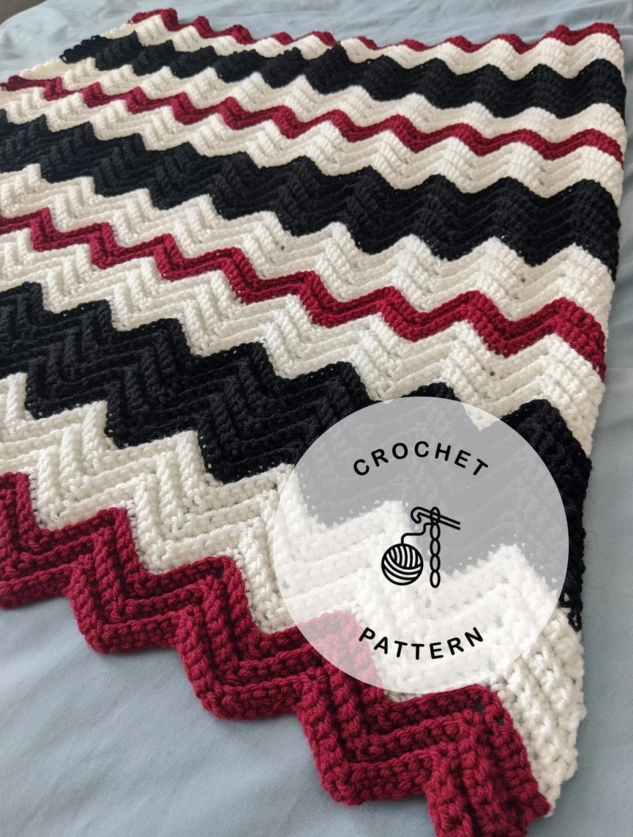 Large red, white, and black chevron zig zag striped crochet blanket folded in half on a bed.