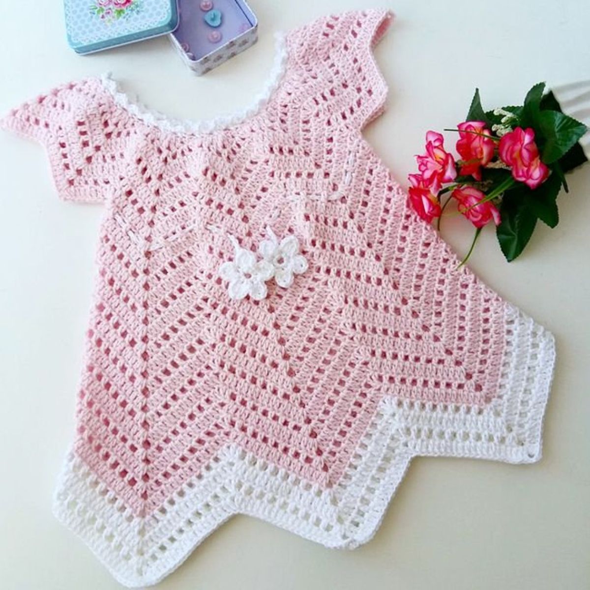 Pink crochet ripple chevron baby dress with short sleeves, white flowers in the middle, and a white zig zag hem.