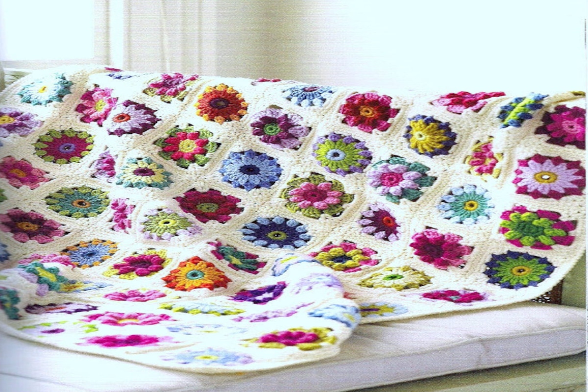 Cream crochet blanket with blue, purple, green, pink, and orange roses and flowers stitched across the blanket and draped over a couch.