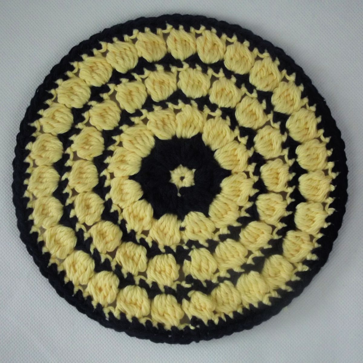 Round black crochet circle with clusters of yellow rows around the design and one small yellow center on a white background.