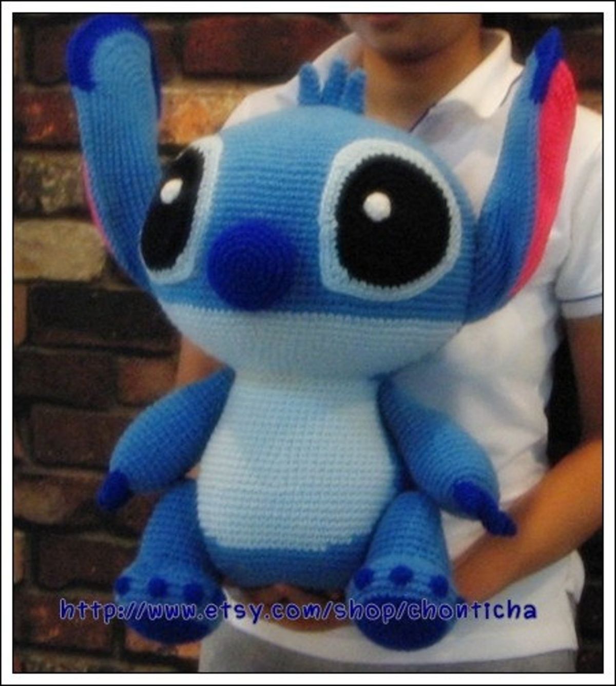 Large crochet stuffed Stitch toy with large black eyes being held by someone with their face out of the shot.