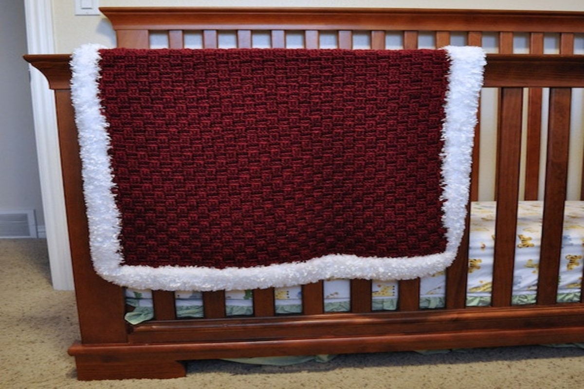  Deep read crochet blanket with a white fluffy trim on all sides draped over a dark wooden bed frame.