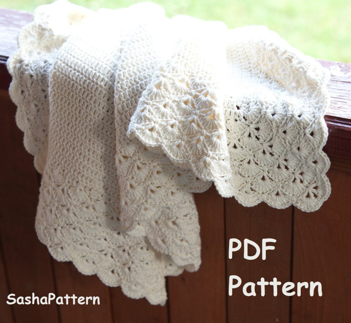 A white crochet lace baby blanket with a scallop edge on all sides bunched up on a wooden fence.