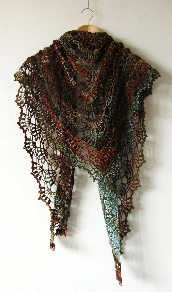 Dark green, orange, and blue lace style crochet shawl wrapped around a wooden hanger on a white background.