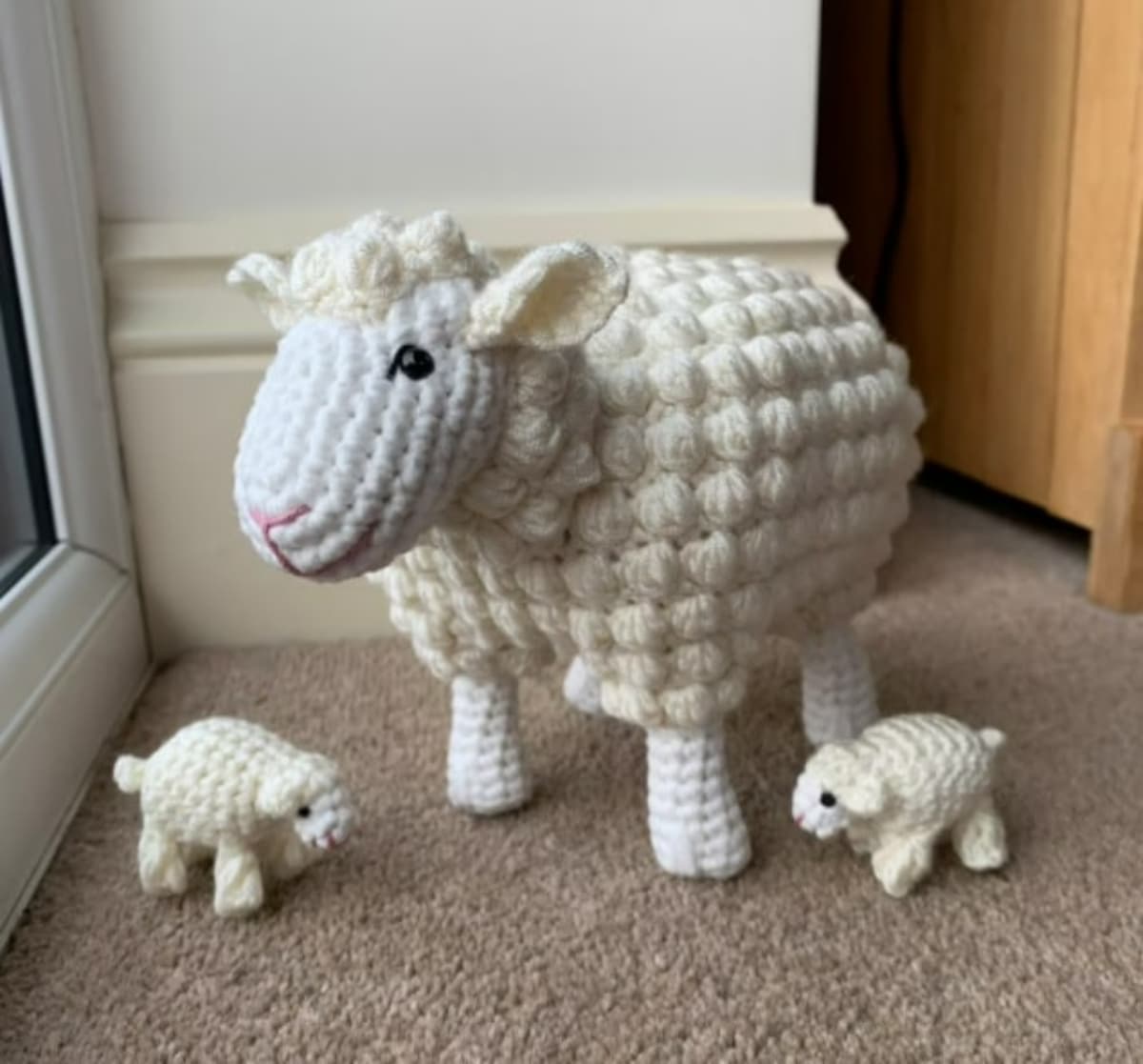 Large white crochet sheep with cream bobbles on its body standing next to two tiny lambs of the same design.